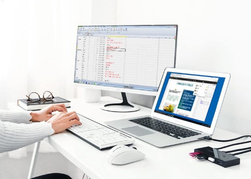 person typing on a desktop computer hooked up to a laptop via a USB switch