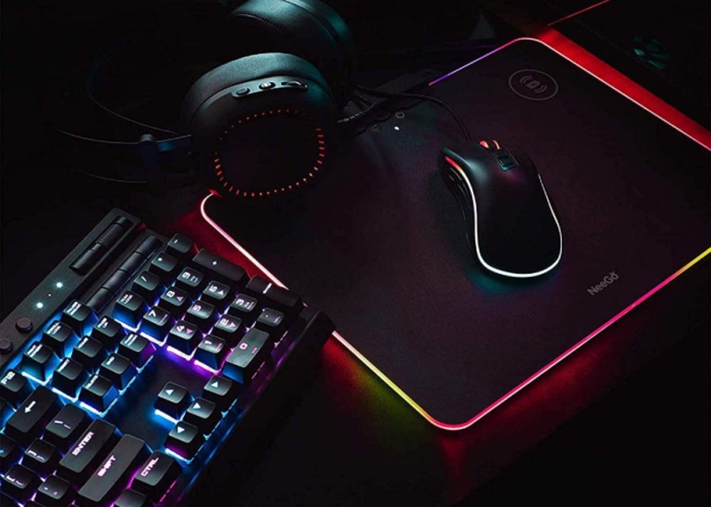 black, rainbow lit charging pad beside a keyboard and supporting a computer mouse