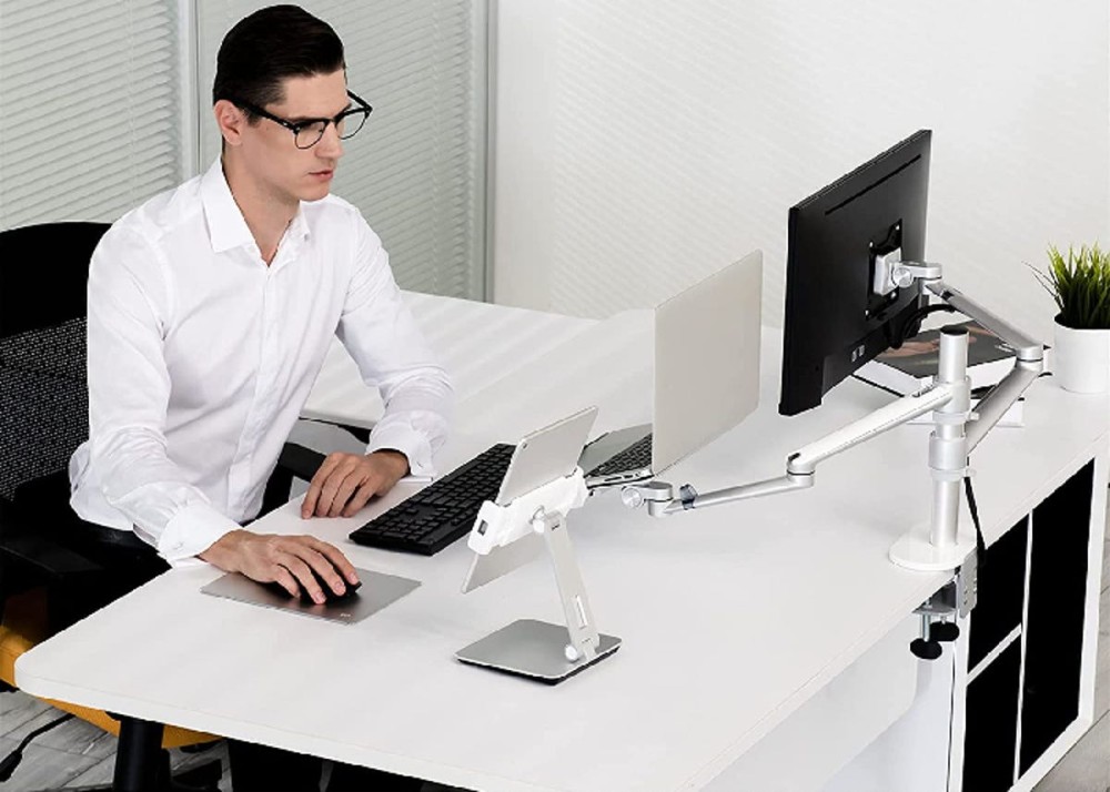 a man sitting at a desk with two monitors set up on a special stand