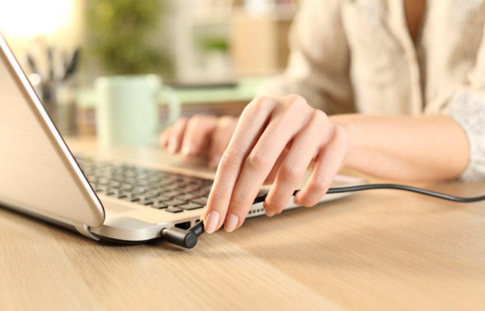 hand plugging in a charger cord to a laptop