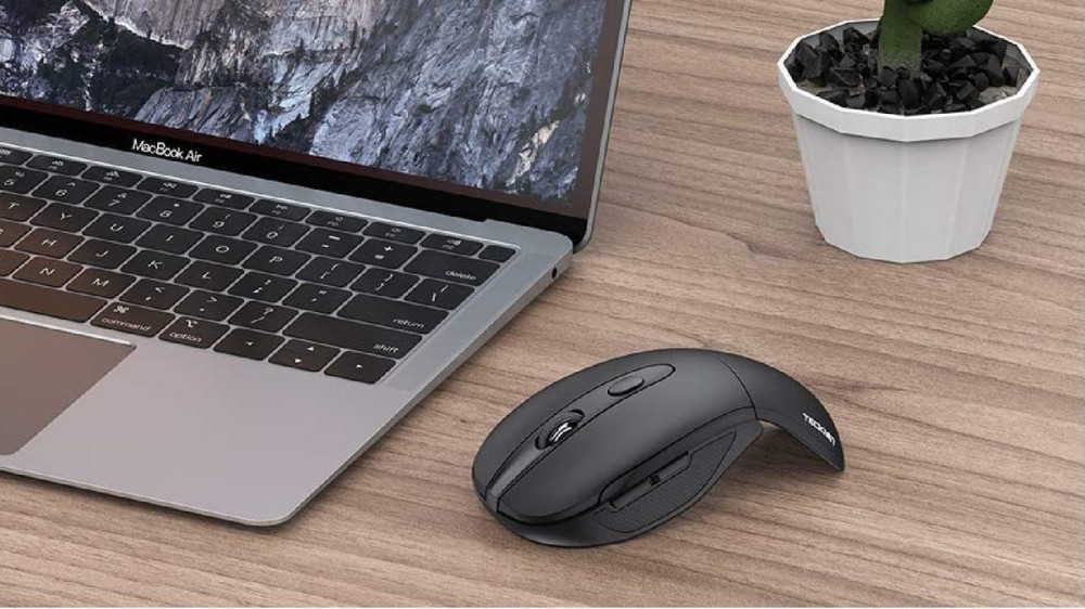 A black arched mouse with buttons next to a laptop.