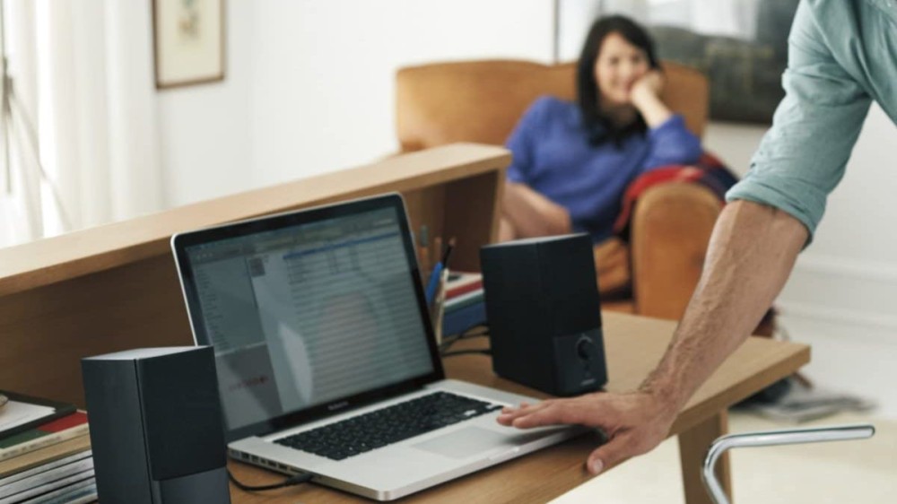 A man uses a laptop that's connected to a stereo computer speaker setup.