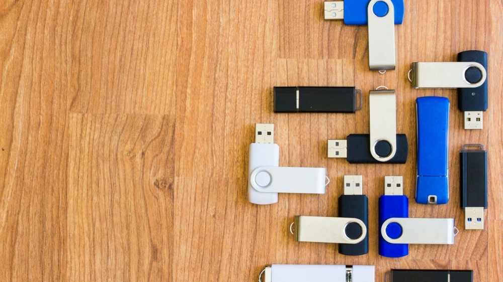 Many USB thumb drives are lined up in different directions on a wooden table.