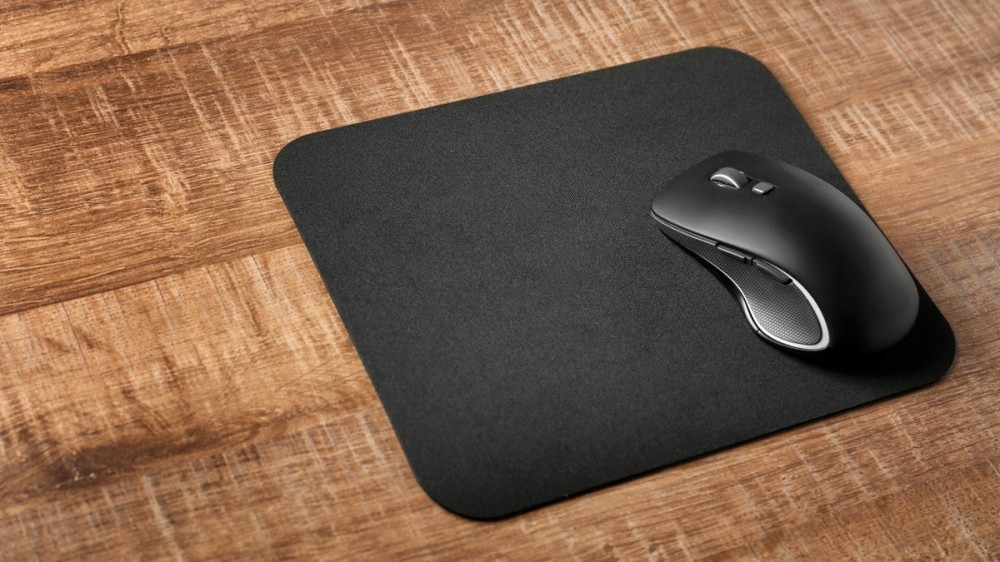 A black mouse pad on a table with a black wireless mouse resting on it.