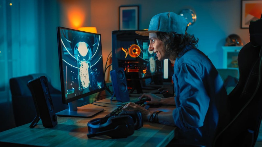 A young man plays video games on his PC in a dark room.