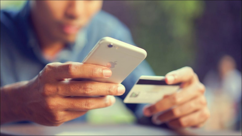 Closeup of a man's hands holding an iPhone and a credit card.