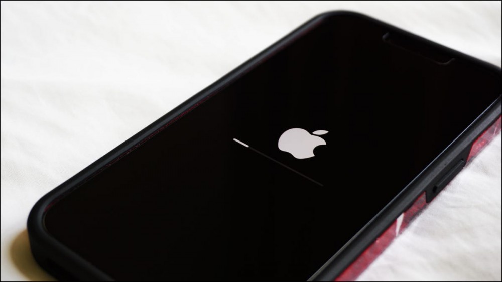 Closeup of an iPhone on a white tabletop with the Apple logo and software upgrade progress bar visible on screen.