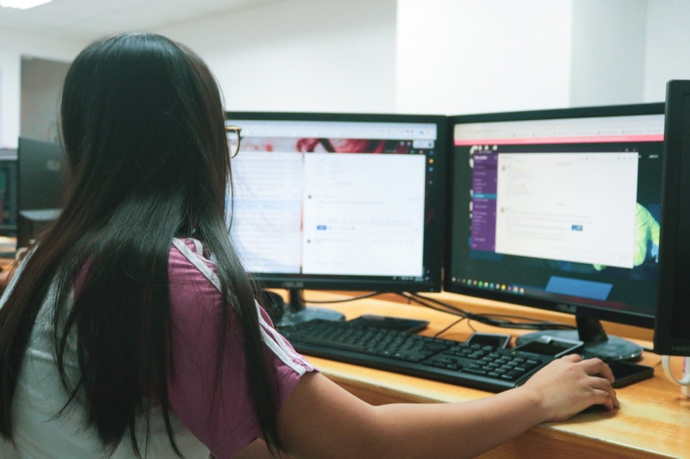 A black-haired woman with glasses using a computer with two monitorsâan excellent use-case for Windows keyboard shortcuts.