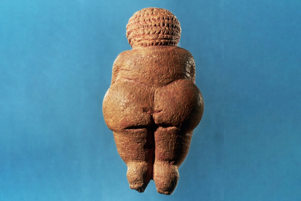 Backside of Benus of Willendorf statue on light blue